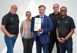 Photo: Simon King (CEO), Nadège Gaverett-Clarke (Project Manager), Dominic Hunter (Company Secretary), Laurence Abbott (CTO), and Justin Ampofo (CFO), holding the official ISO 9001 certificate.